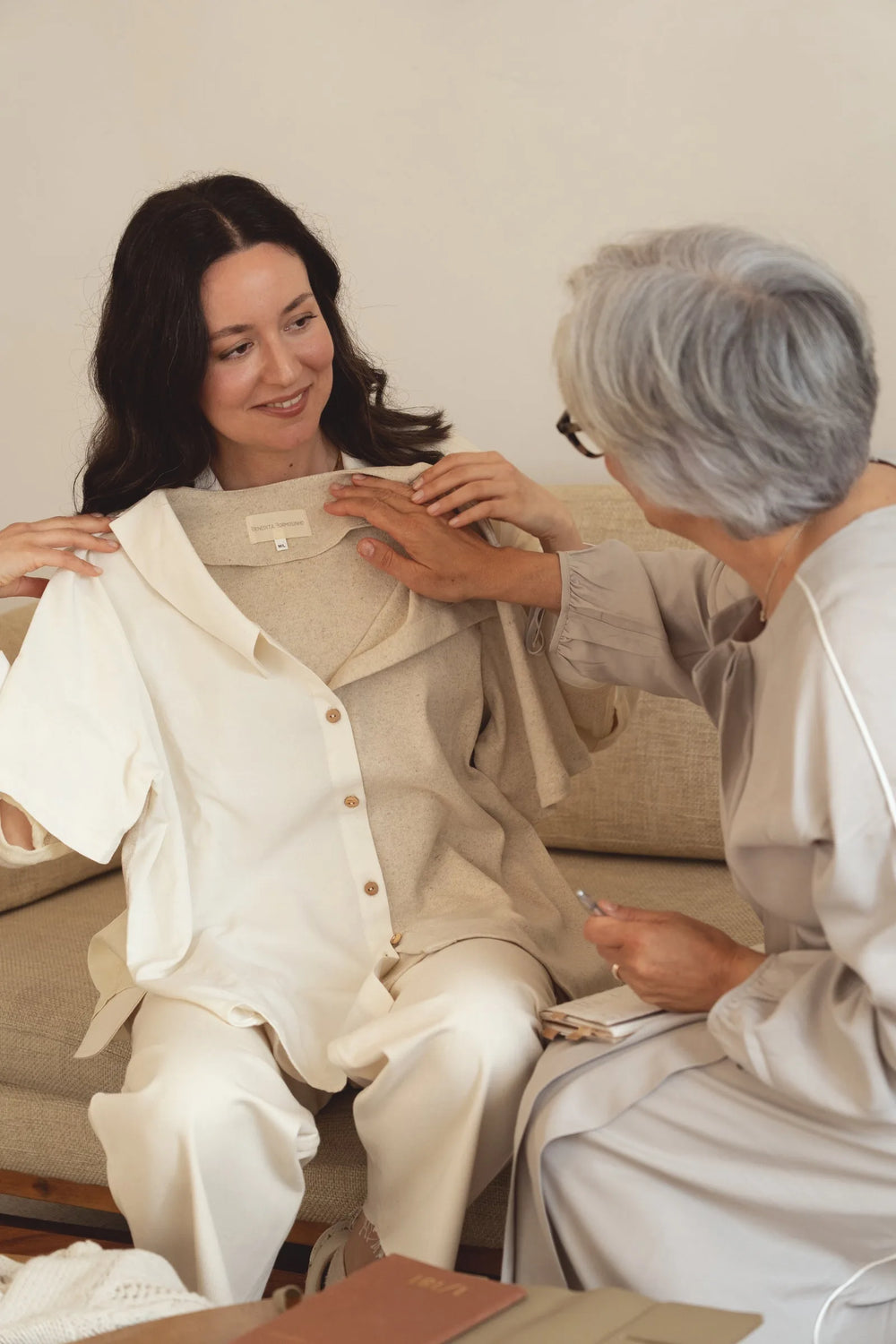 Duas mulheres a avaliar uma peça de roupa em tons neutros no atelier